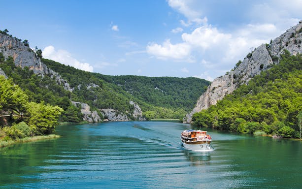 Boat cruising through Krka National Park's lush canyon, Croatia.