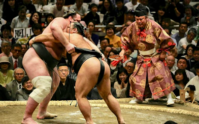 Sumo wrestlers competing at Grand Sumo Tournament in Japan with referee observing.