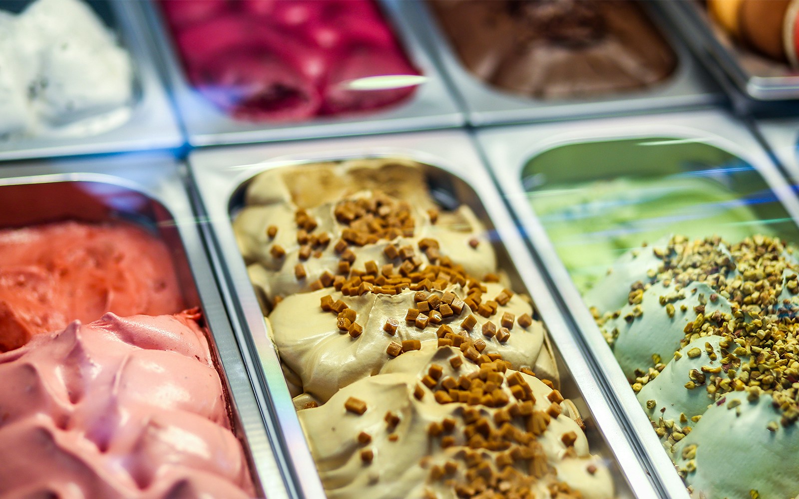 Assorted gelato tubs with various flavors and toppings in a display case.