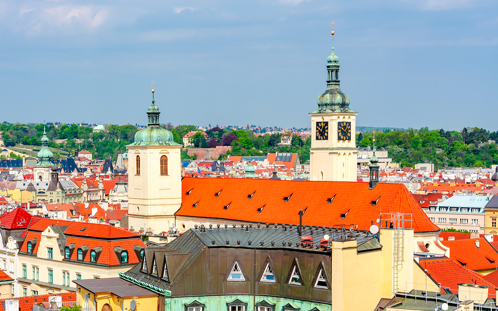 Basilica of St. James towers over Prague's historic skyline with red rooftops and green domes.