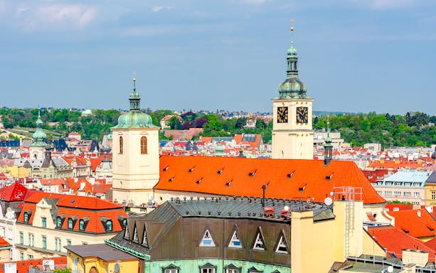 Basilica of St. James towers over Prague's historic skyline with red rooftops and green domes.