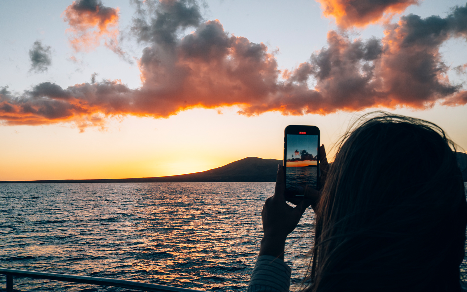 Tourist capturing Lanzarote sunset over ocean with smartphone.