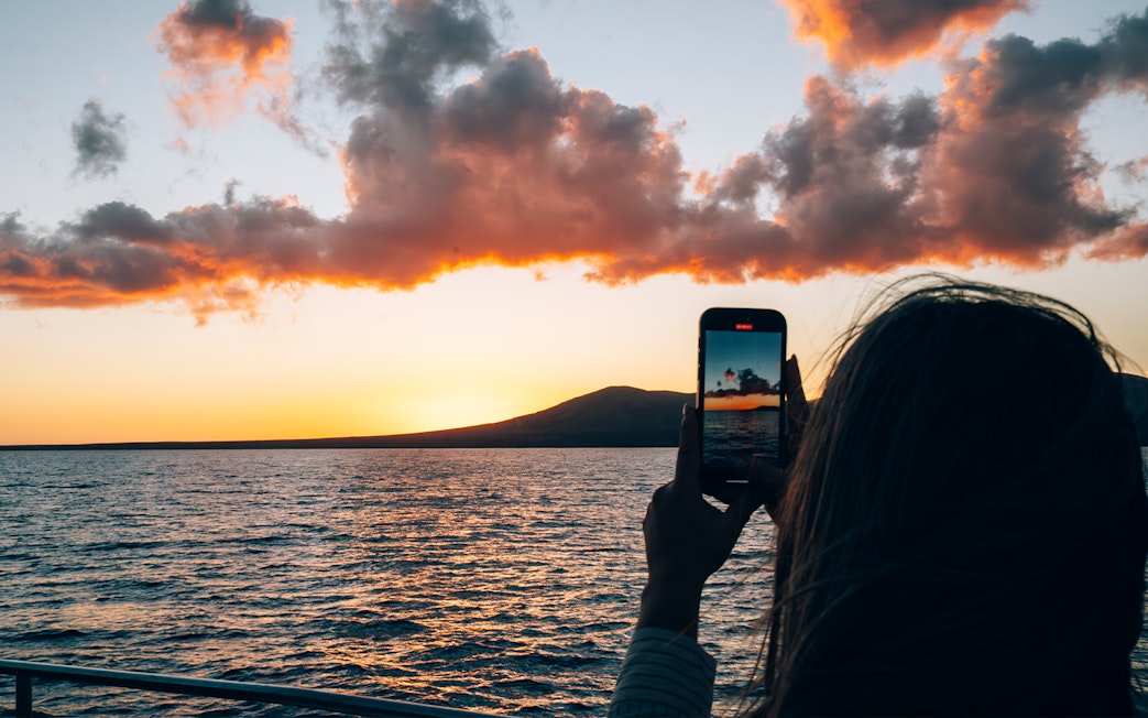 Tourist capturing Lanzarote sunset over ocean with smartphone.
