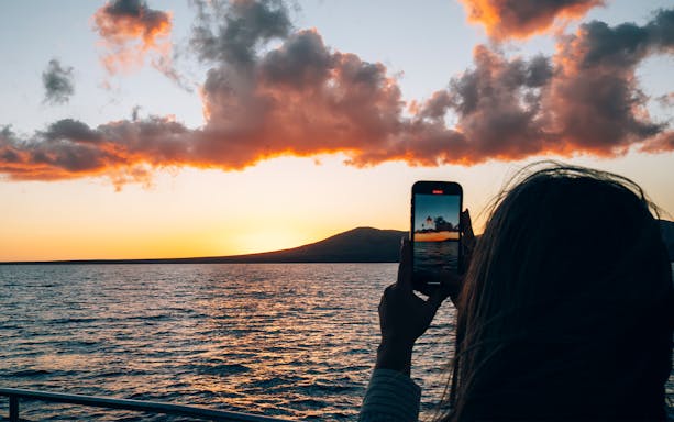 Tourist capturing Lanzarote sunset over ocean with smartphone.