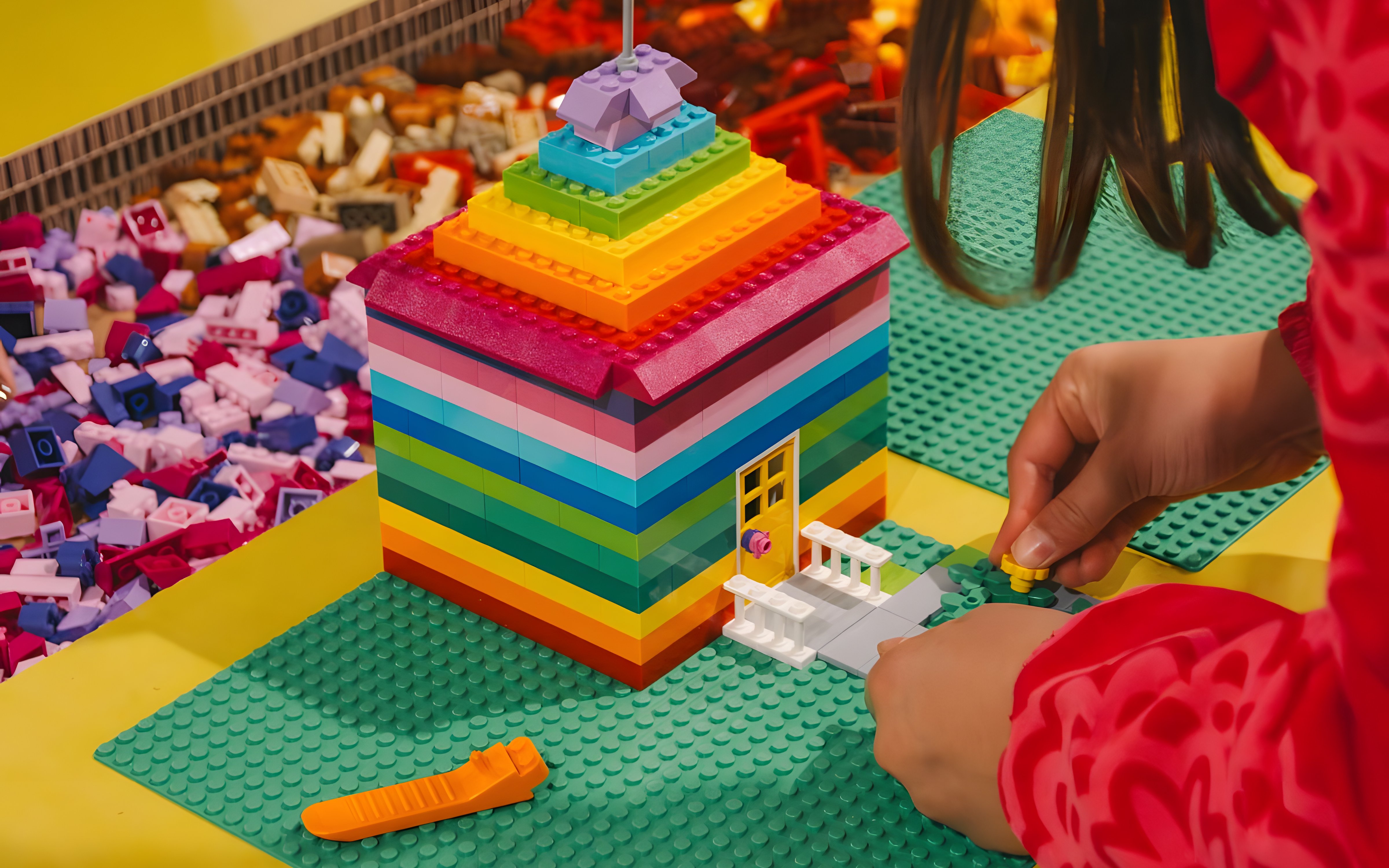 Child assembling a colorful LEGO house at BrickWorld exhibition, WOW Porto.