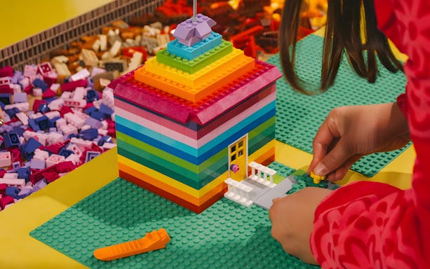 Child assembling a colorful LEGO house at BrickWorld exhibition, WOW Porto.