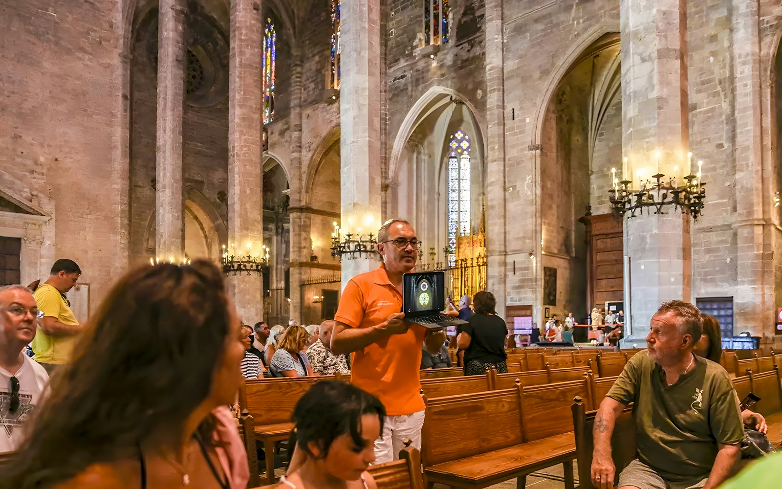 Tour guide explaining to visitors inside Palma Cathedral with stained glass windows.