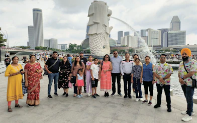 Group of tourists at Merlion Park with Singapore skyline in the background.