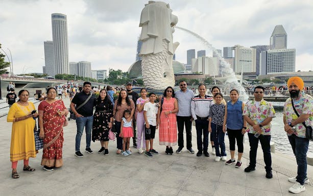 Group of tourists at Merlion Park with Singapore skyline in the background.