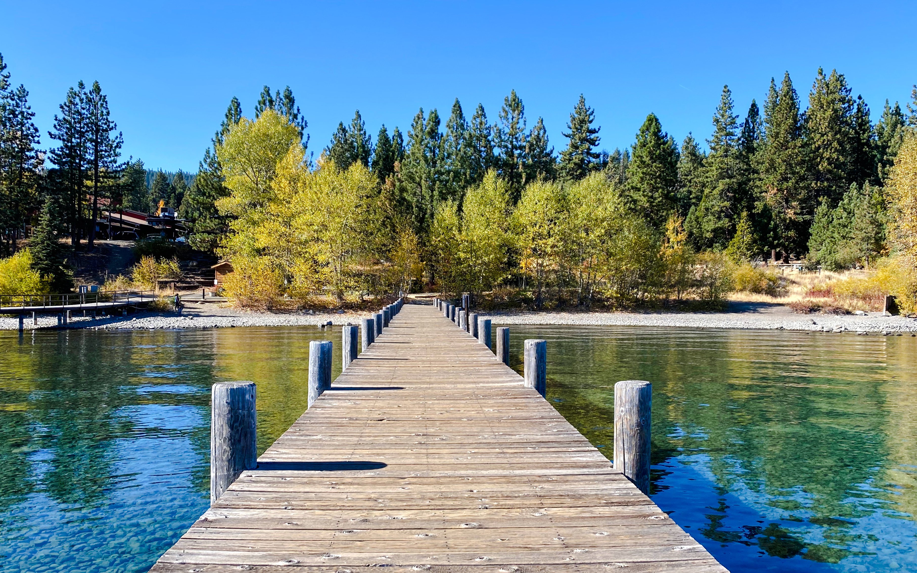 Wooden pier extending into a clear lake with autumn trees in the background.