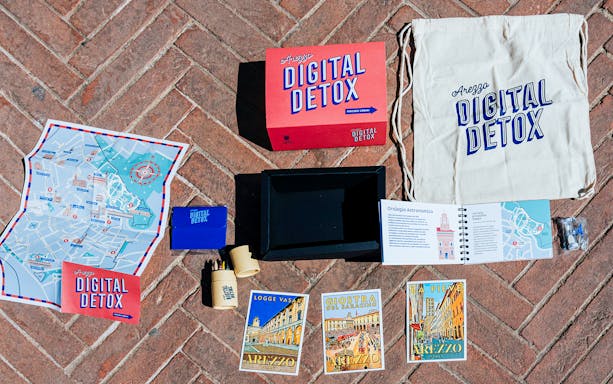 Arezzo Digital Detox tour kit with map, postcards, and guidebook on brick pavement.