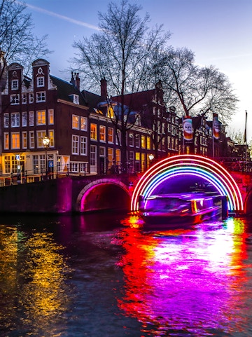 Canal boat under illuminated rainbow arch at Amsterdam Light Festival.