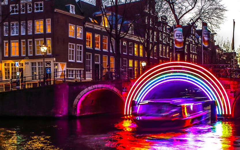 Canal boat under illuminated rainbow arch at Amsterdam Light Festival.