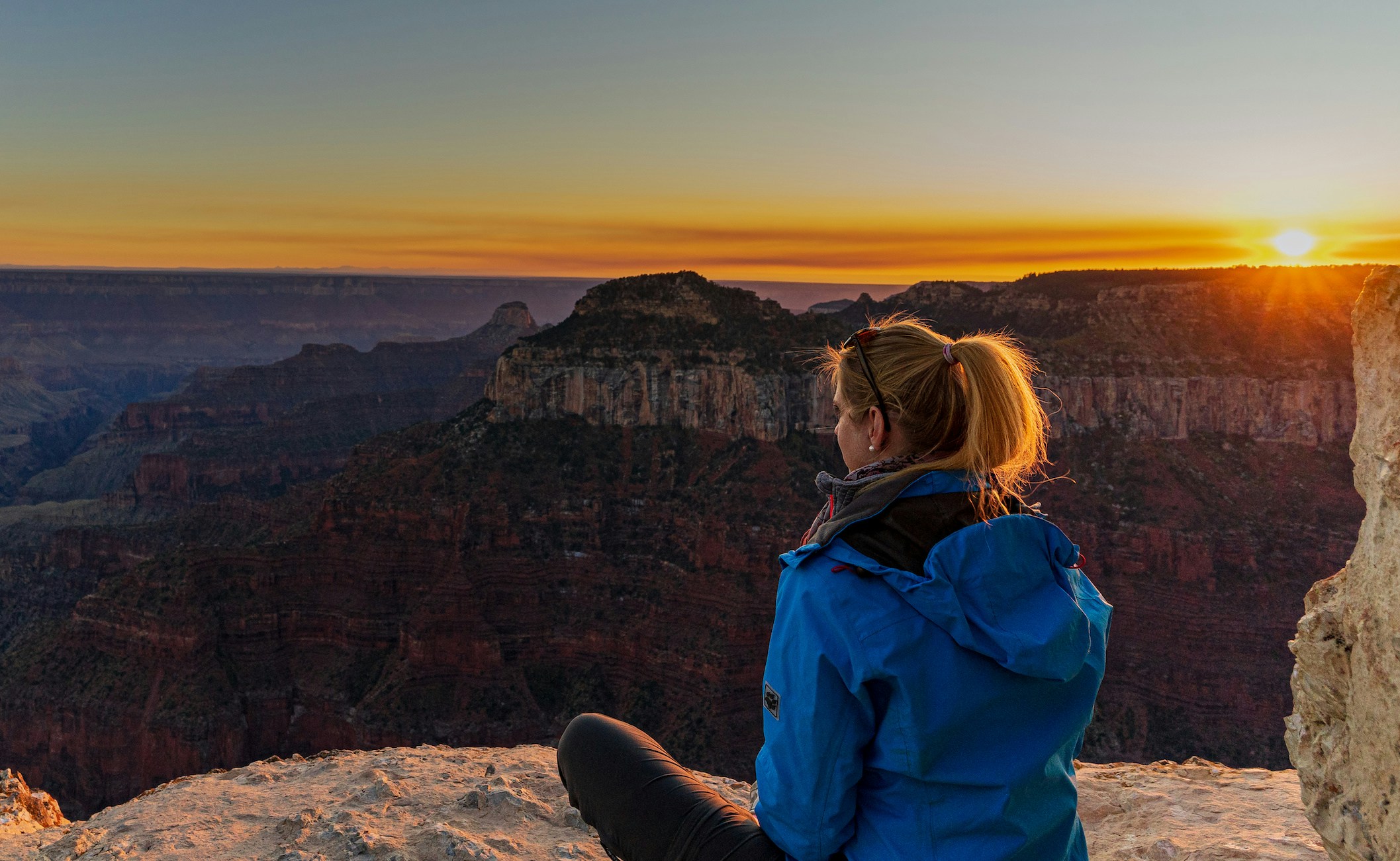 Person sitting at North Rim, Grand Canyon, watching sunset over canyon landscape.