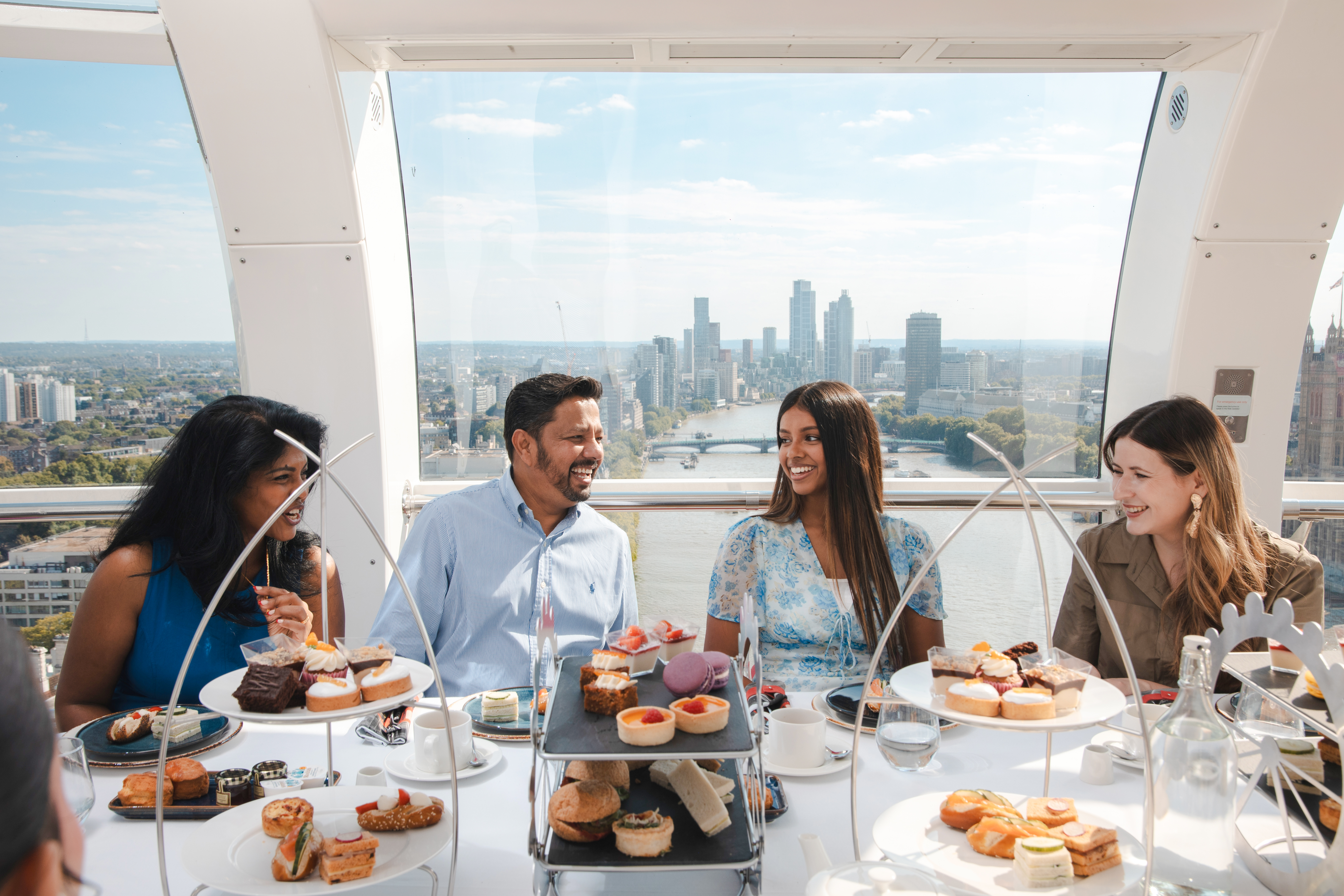 Group enjoying afternoon tea inside the London Eye with city skyline view.