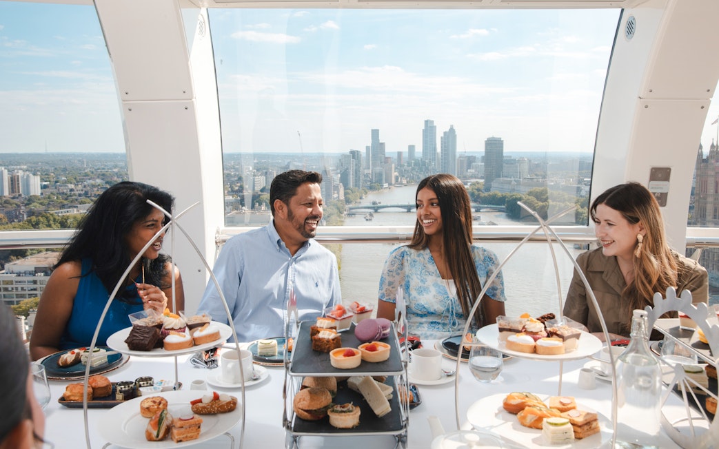 Group enjoying afternoon tea inside the London Eye with city skyline view.