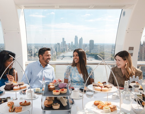 Group enjoying afternoon tea inside the London Eye with city skyline view.