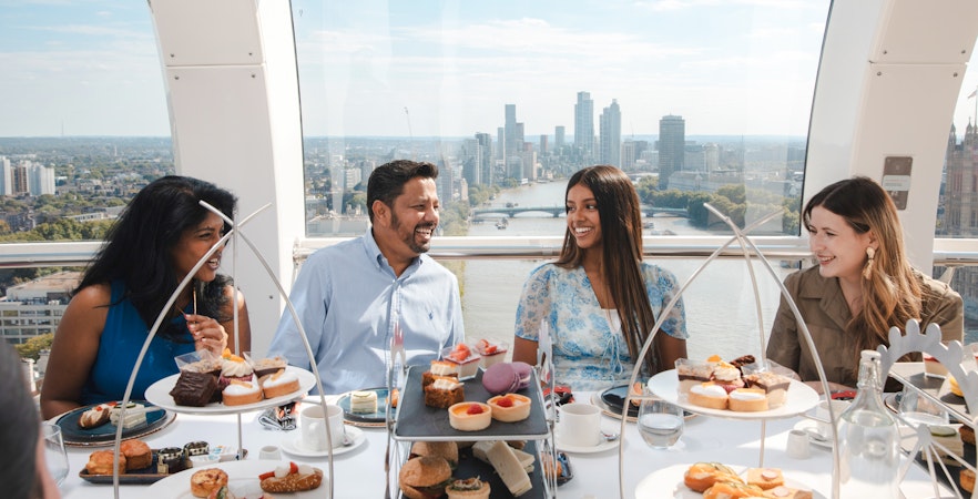 Group enjoying afternoon tea inside the London Eye with city skyline view.