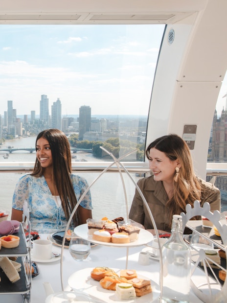 Group enjoying afternoon tea inside the London Eye with city skyline view.