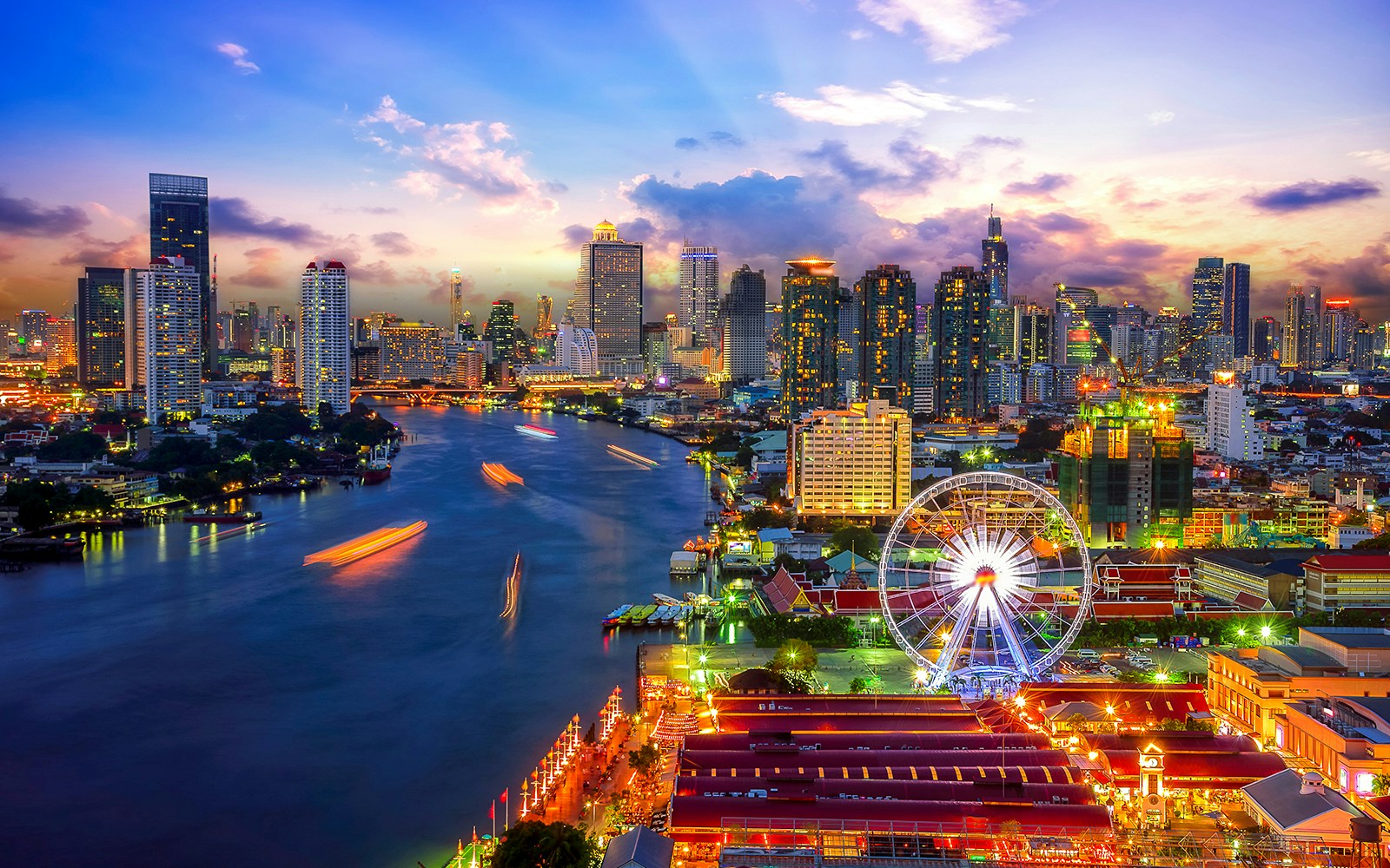 Bangkok skyline with Asiatique riverfront and Ferris wheel at sunset.