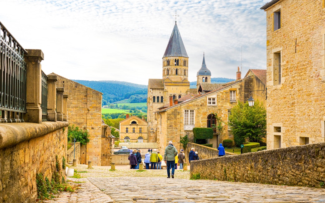 Cluny Abbey in Lyon, France with tourists walking on cobblestone street.