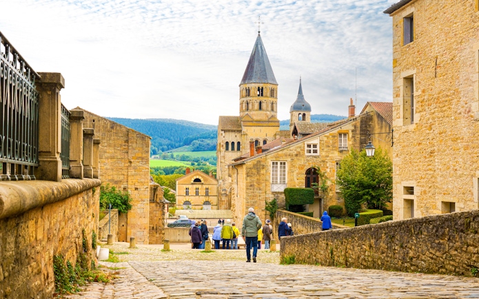 Cluny Abbey in Lyon, France with tourists walking on cobblestone street.