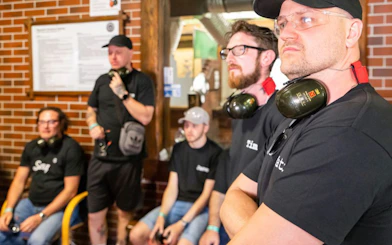 Group of people at an indoor shooting range with ear protection, part of an extreme shooting tour.