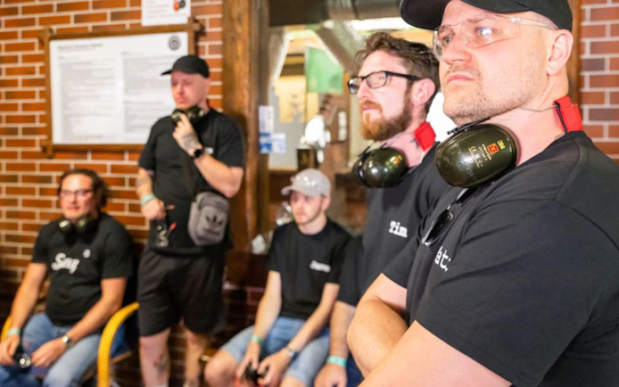 Group of people at an indoor shooting range with ear protection, part of an extreme shooting tour.