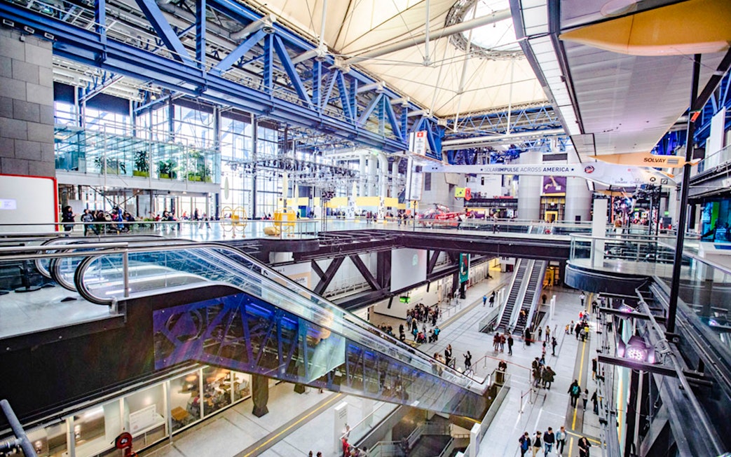 Interior view of Science & Industry Museum, Paris, featuring escalators and visitors.