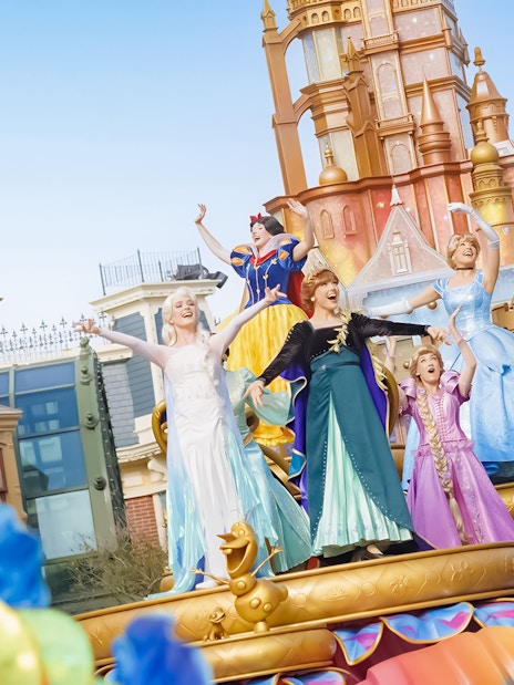 Princesses on a colorful float at Friendtastic! Parade with castle backdrop.