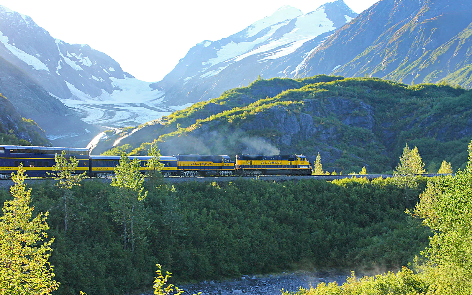 Alaska Railroad train traveling through scenic mountain landscape with snow-capped peaks.
