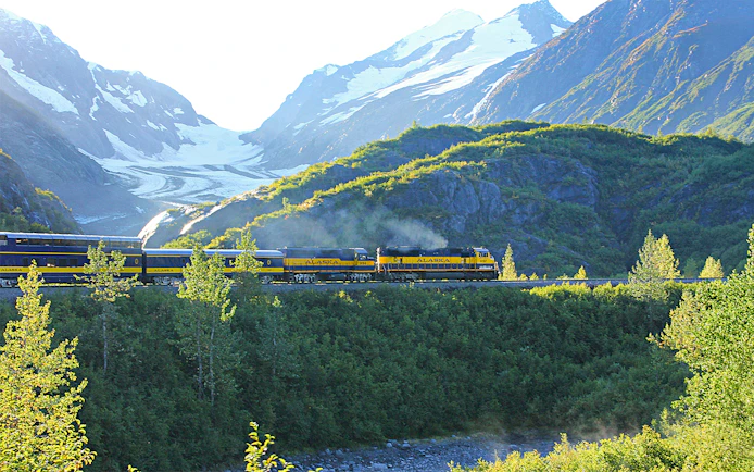 Alaska Railroad train traveling through scenic mountain landscape with snow-capped peaks.