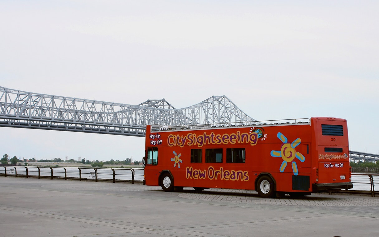 New Orleans Hop-On Hop-Off bus near a bridge along the riverfront.