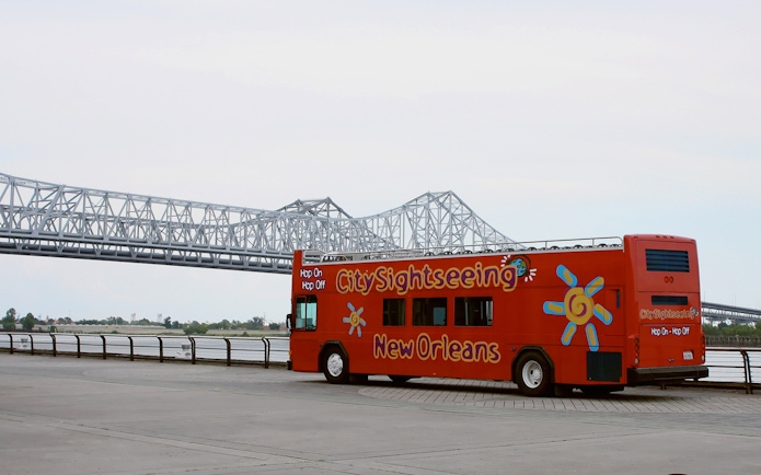 New Orleans Hop-On Hop-Off bus near a bridge along the riverfront.