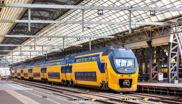 Amsterdam train crossing a bridge over a canal with historic buildings in the background.