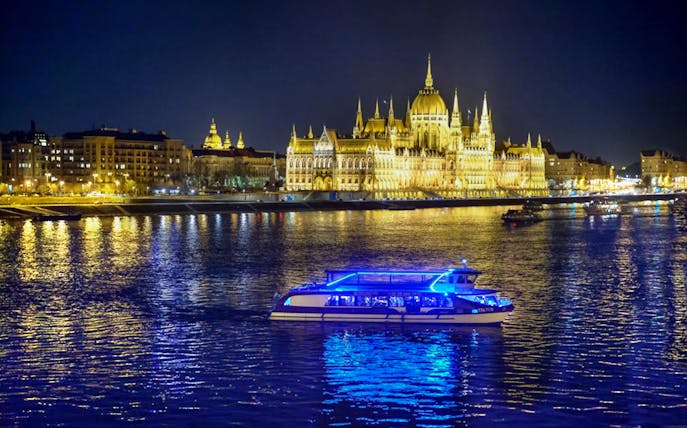 Cruise boat on the Danube River with Budapest Parliament lit up at night.