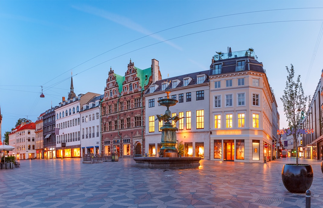 Stork Fountain in Copenhagen's Amagertorv Square surrounded by historic buildings at dusk.