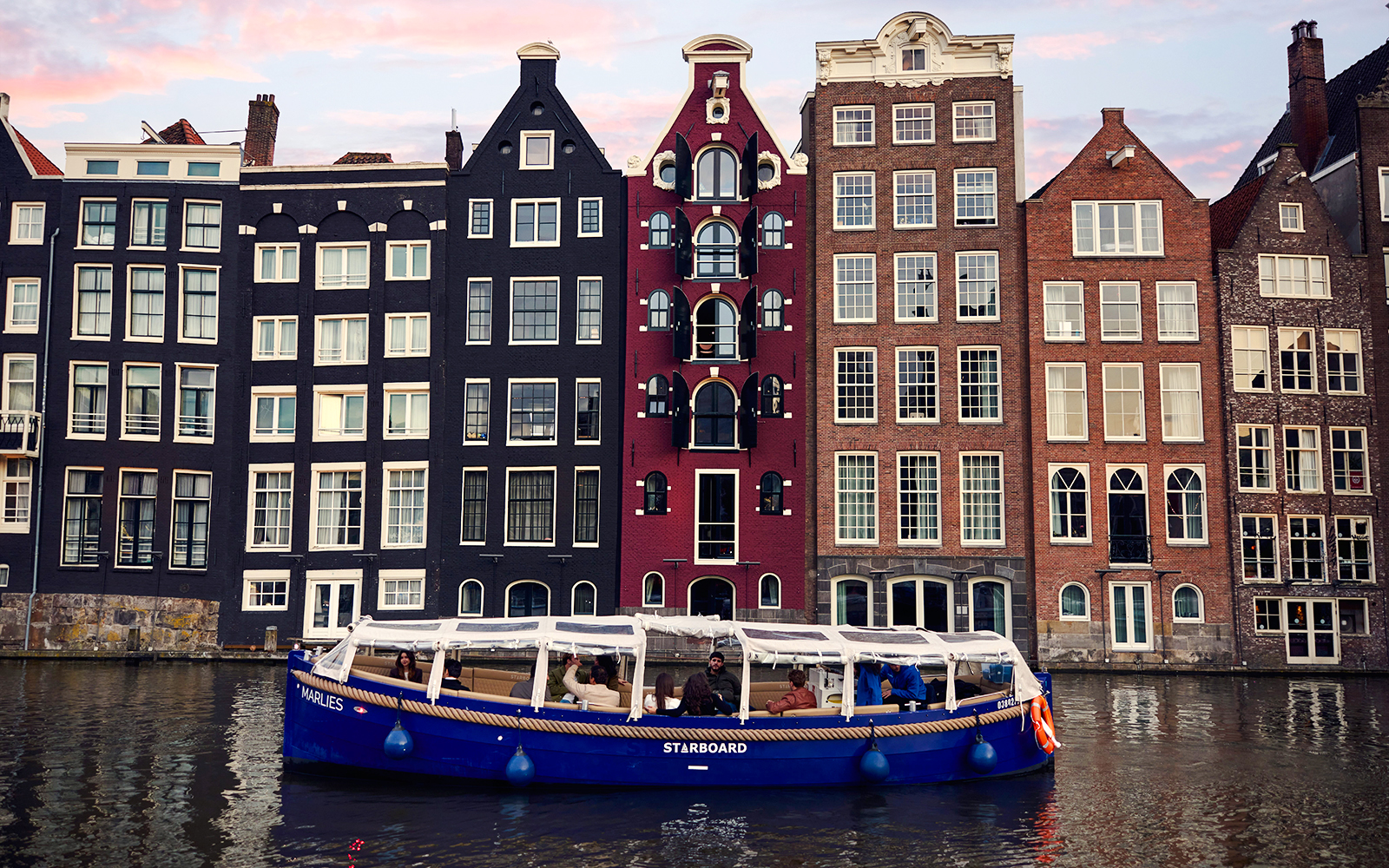 Amsterdam canal cruise boat with passengers, historic canal houses in the background.