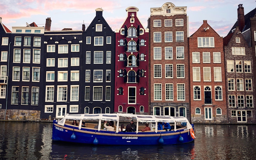 Amsterdam canal cruise boat with passengers, historic canal houses in the background.