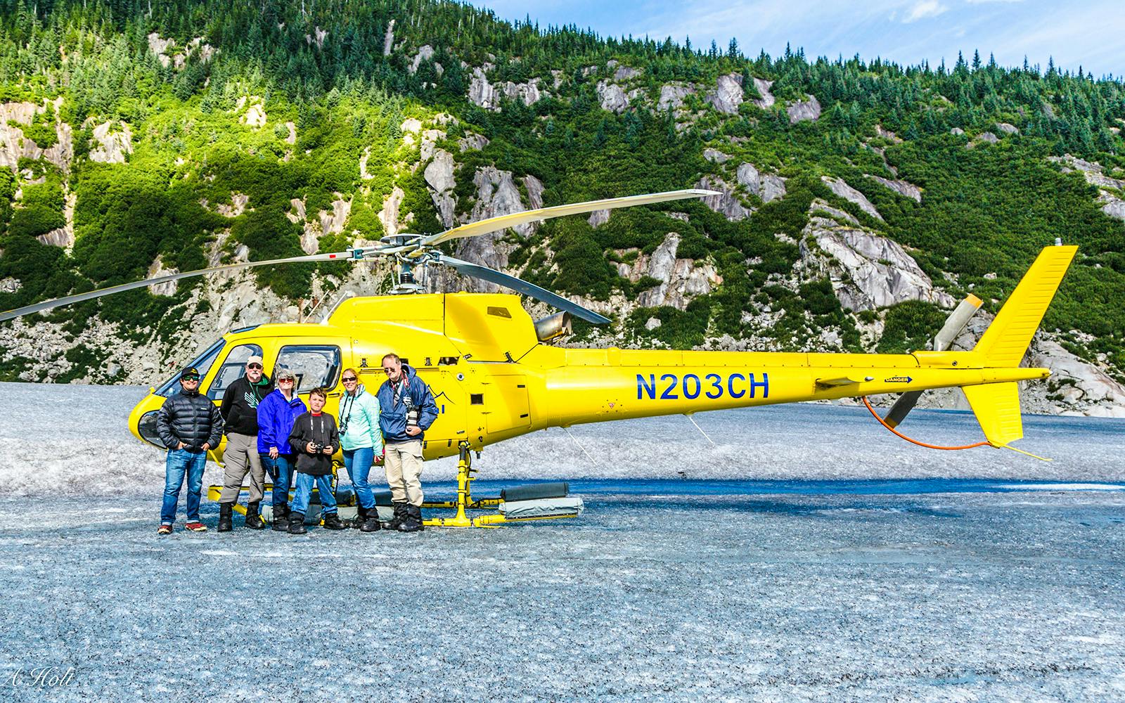 Group beside yellow helicopter on glacier during Juneau tour with dog sledding.