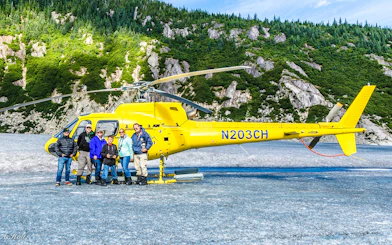Group beside yellow helicopter on glacier during Juneau tour with dog sledding.