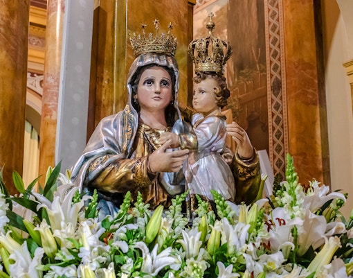 Statue of crowned figures surrounded by flowers in a church setting.
