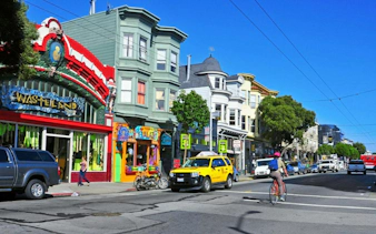 Colorful storefronts and street scene in Haight Ashbury, San Francisco, with cyclist and taxi.