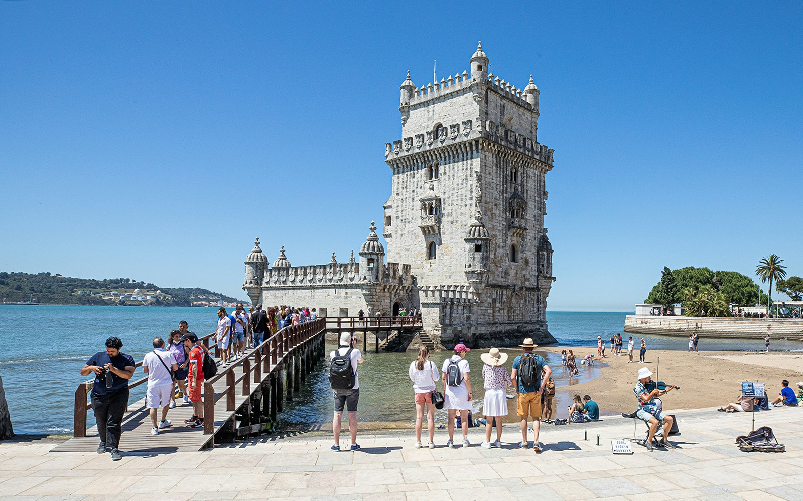 Tourists visiting Belém Tower in Lisbon, Portugal, with a musician playing nearby.