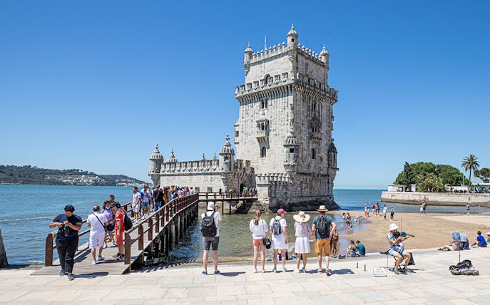Tourists visiting Belém Tower in Lisbon, Portugal, with a musician playing nearby.