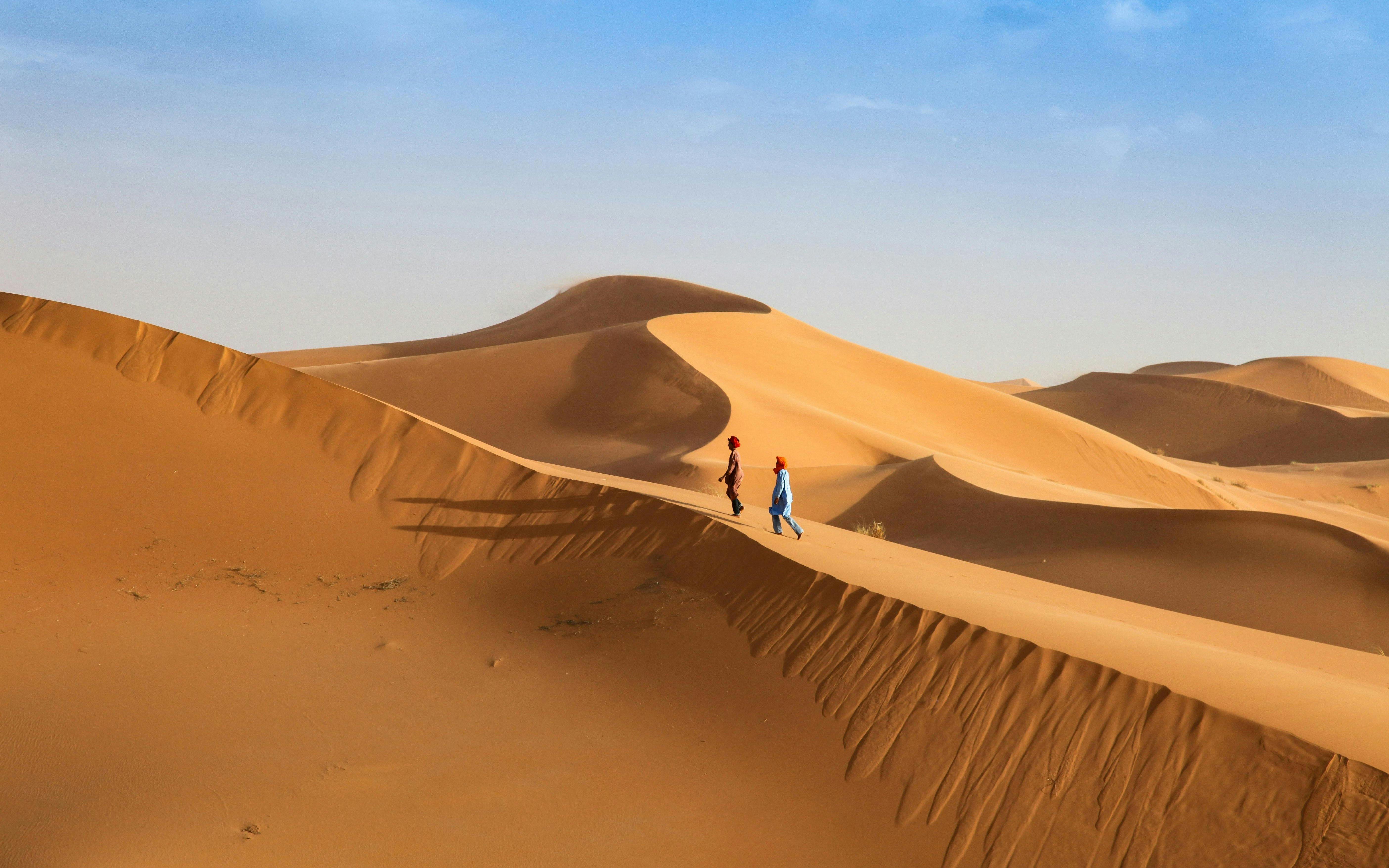 Young men walking across sand dunes in a desert landscape.