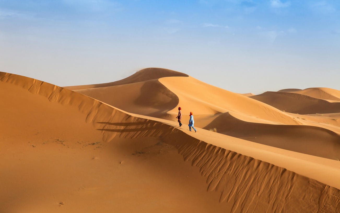 Young men walking across sand dunes in a desert landscape.