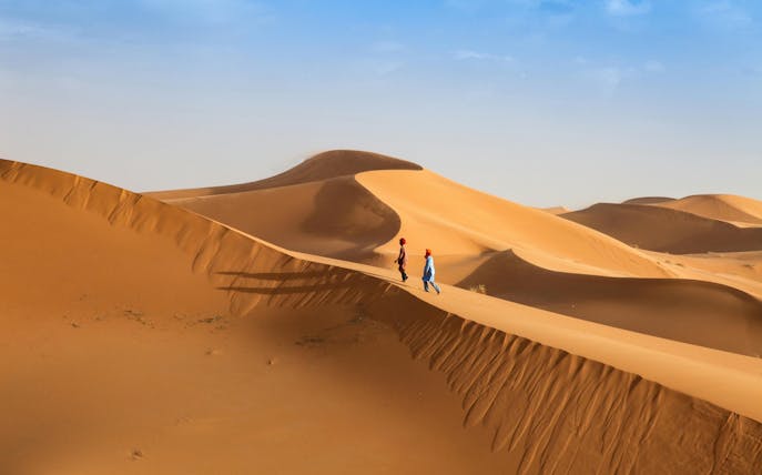Young men walking across sand dunes in a desert landscape.
