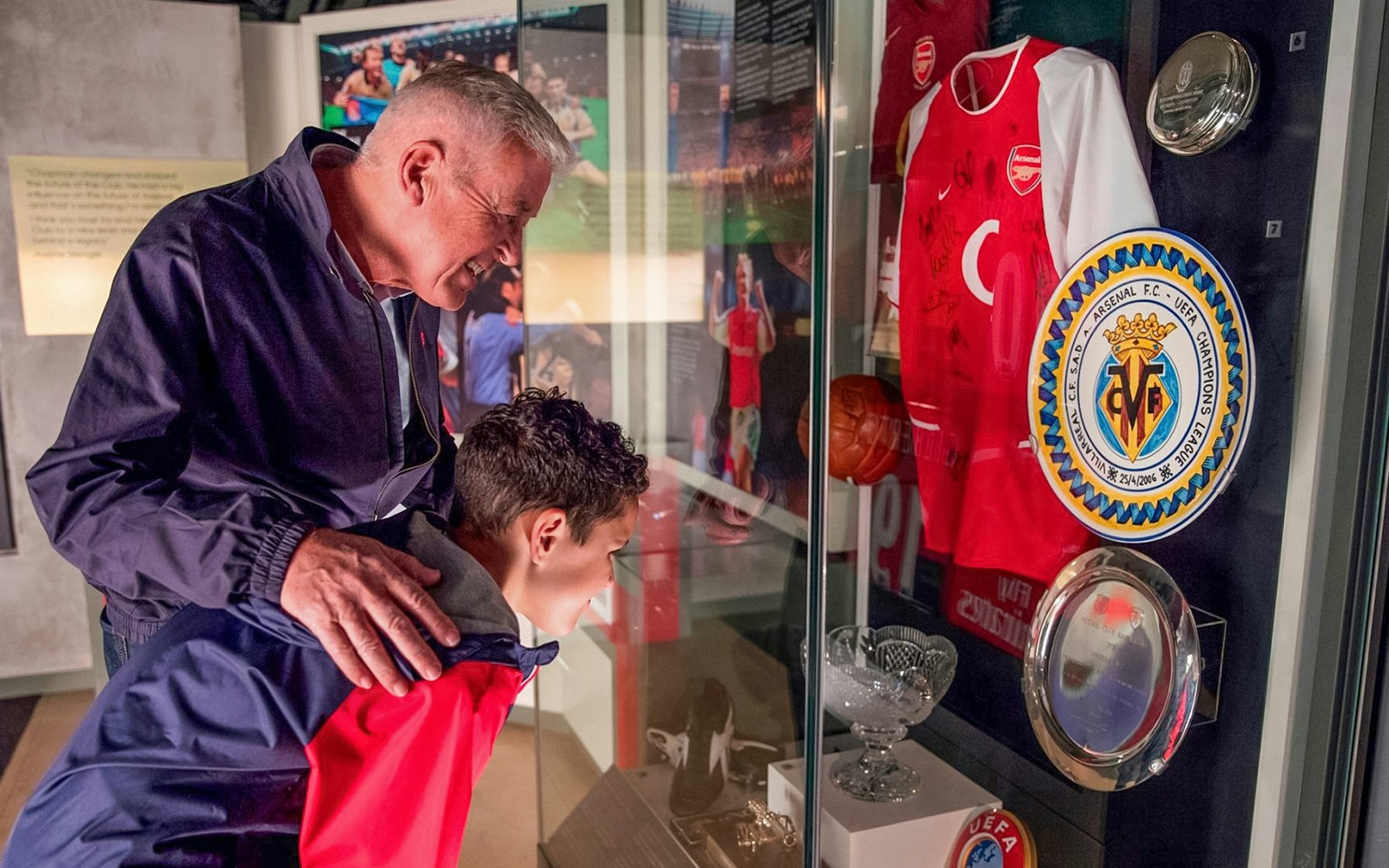 Visitors examining Arsenal memorabilia at Emirates Stadium tour display.