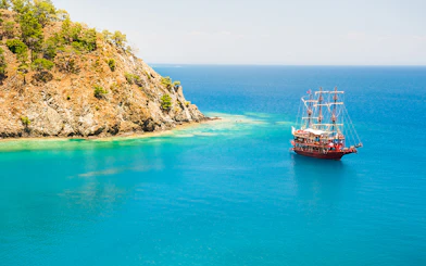 Boat sailing near rocky coastline in Phaselis during a guided tour from Antalya.